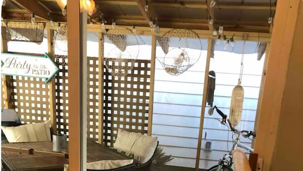 Una terraza de madera con mobiliario de mimbre, una bicicleta y un letrero que dice 'Party on the Patio'.