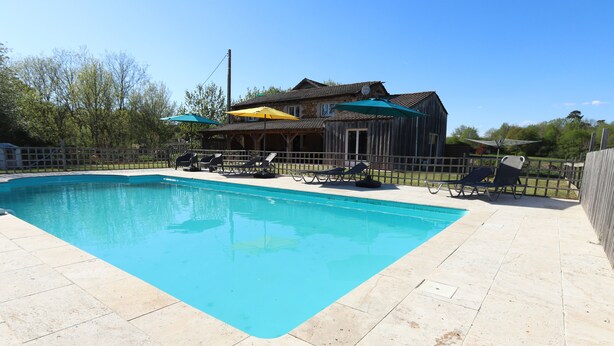 A swimming pool with lounge chairs and umbrellas, surrounded by a wooden fence.