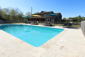 A swimming pool with lounge chairs and umbrellas, surrounded by a wooden fence. - Le Magnolia, 4 bedroom house with private pool in the Lot et Garonne (Lacapelle-Biron)