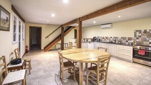 A spacious kitchen with a wooden dining table and chairs, a staircase, and a tiled backsplash.