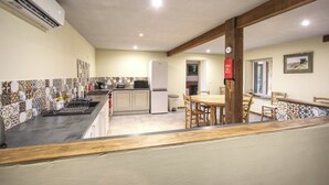 A kitchen with a microwave, stove, and refrigerator. There is a dining table with chairs and a wooden beam ceiling.