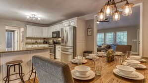 A modern kitchen with white cabinetry, stainless steel appliances, and a wooden dining table set for six. - Tranquility Hollow Private INDOOR POOL, WIFI, next to Dollywood (Sevierville)