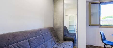 A room with a grey sofa, a blue chair, a sliding door, and a window with a view of greenery outside.