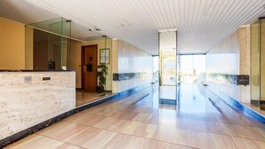 Un vaste hall d’entrée doté d’un sol en marbre, de murs en verre et d’une porte en bois au fond.