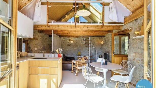 A rustic kitchen with wooden cabinets, a stone wall, and a dining area with white chairs and a round table.