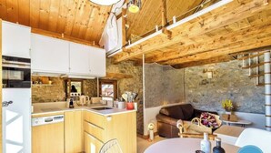 A compact kitchen with wooden cabinets, a stone wall, and a dining area with a table and chairs.