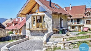 A stone building with a wooden balcony, a stone staircase, and a paved driveway.