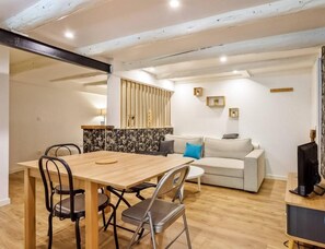 A modern living room with a wooden dining table, a sofa, and a TV. - Les Amandiers - T1 apartment (TALLOIRES)