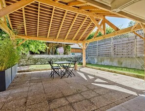 A covered patio area with a table and chairs, surrounded by stone walls and greenery. - Les Amandiers - T1 apartment (TALLOIRES)