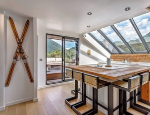 Une cuisine moderne avec un îlot central en bois, de grandes fenêtres et une vue sur les montagnes.