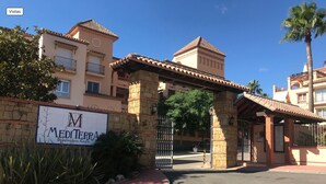 Une entrée fermée par un portail mène à un hôtel de style méditerranéen, doté d’une façade en pierre et d’un toit recouvert de tuiles.