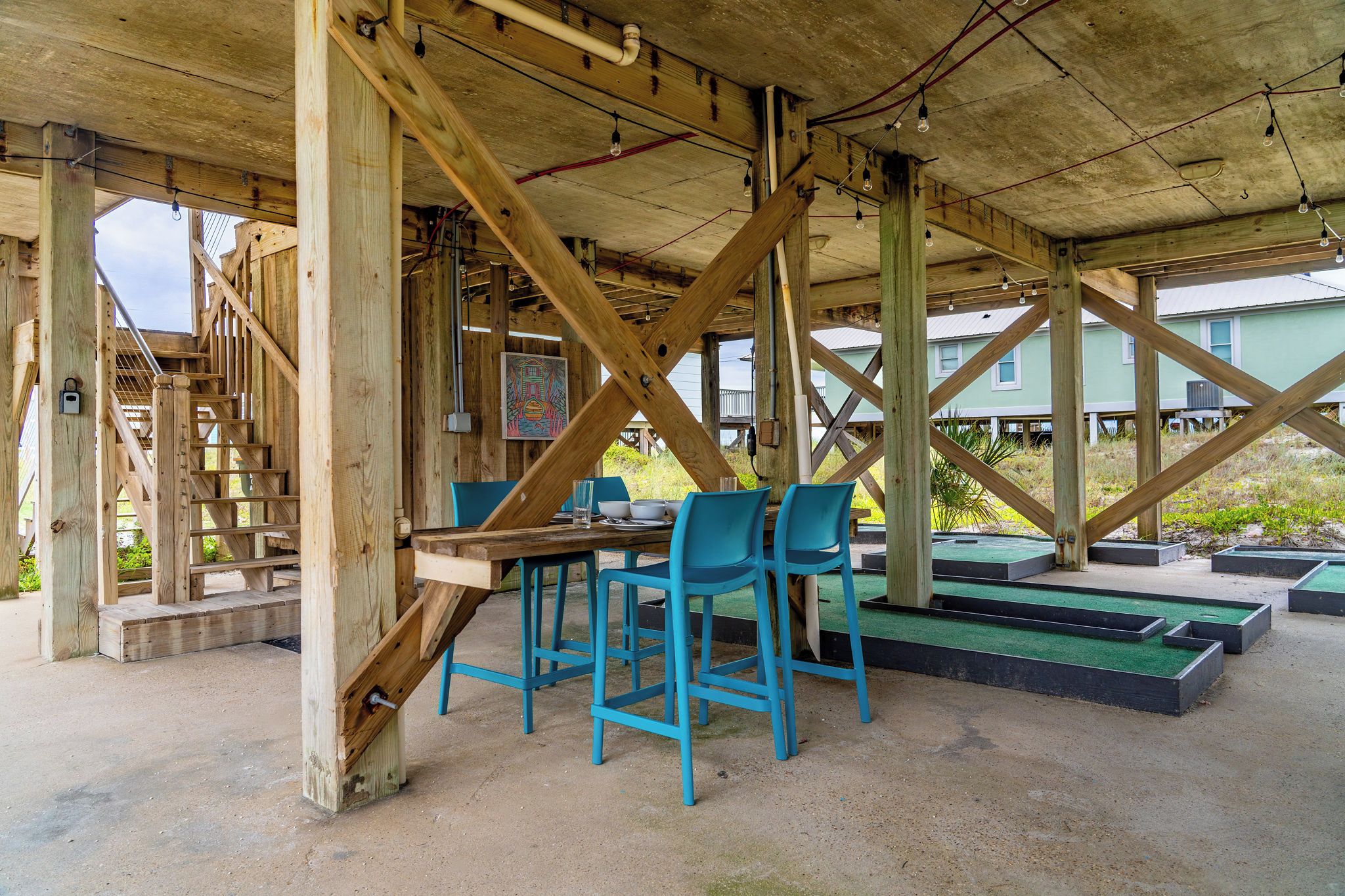 A wooden structure with a table and chairs, a staircase, and a green outdoor area with planters.