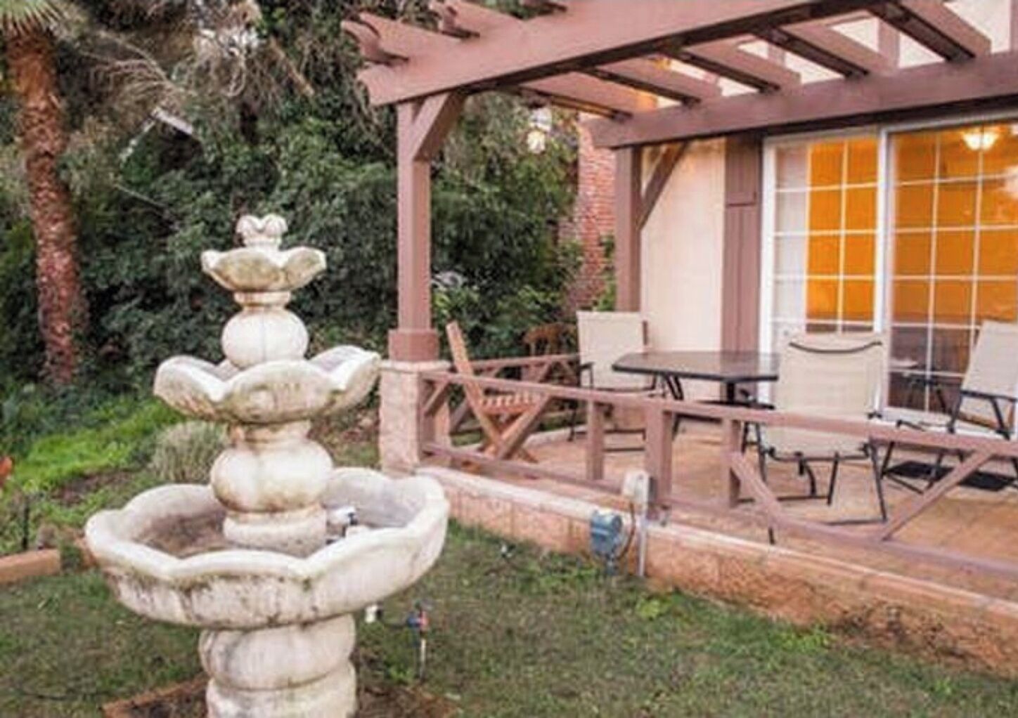 A patio area with a stone fountain, outdoor seating, and a pergola.