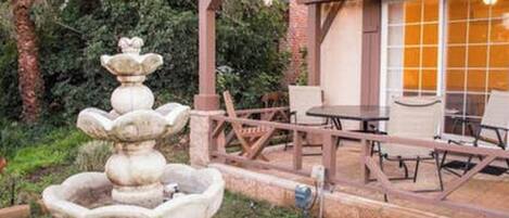 A patio area with a stone fountain, outdoor seating, and a pergola.