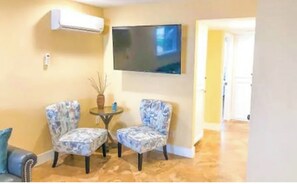A living room with two patterned armchairs, a small round table, and a flat-screen TV mounted on the wall. - STEPS TO OCEAN, NEW,CLEAN #2 (Oceanside)
