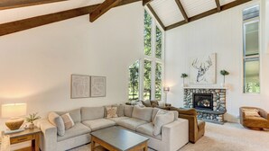 Un salon spacieux doté d’un grand canapé d’angle, d’une cheminée et de grandes fenêtres offrant une vue sur l’extérieur.