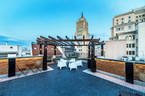 A rooftop terrace with a pergola, white chairs, and a brick wall.