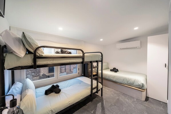A bunk bed room with a window, a small desk, and a wardrobe.