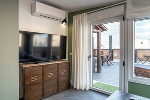 Un espace de vie moderne doté d’un téléviseur à écran plat fixé à un meuble, d’une porte-fenêtre coulissante donnant sur un espace extérieur et d’un appareil de climatisation visible.