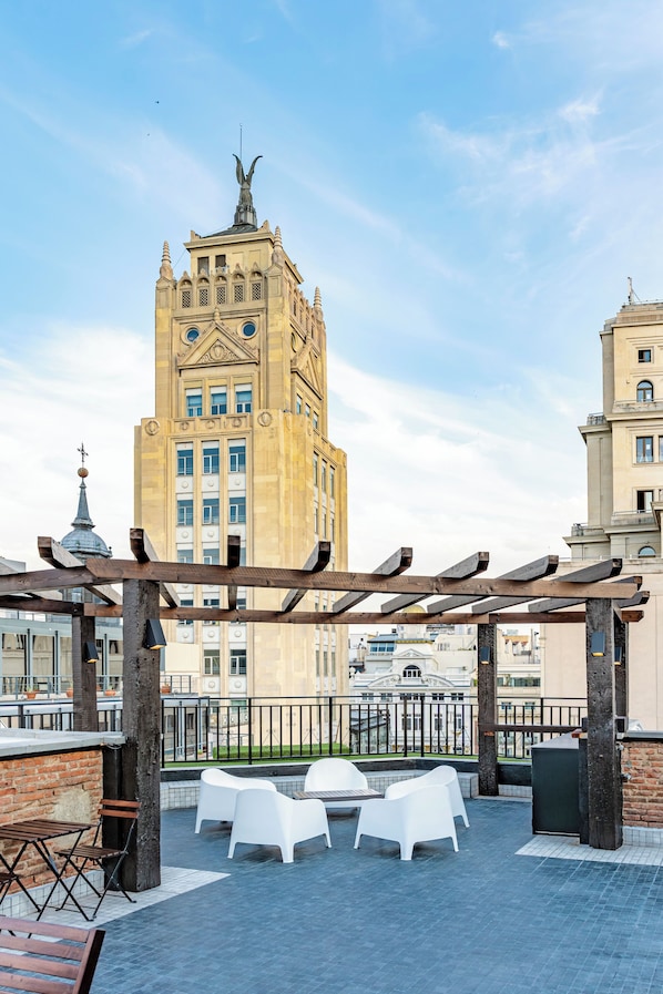 Terraza en la azotea con mobiliario exterior, una pérgola y vistas a un edificio histórico con una estatua.