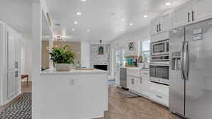 A modern kitchen with white cabinetry, a central island, a stainless steel refrigerator, and a herringbone wood floor. - Catalina Hideaway - Heated Pool - Game Room (Indian Harbour Beach)