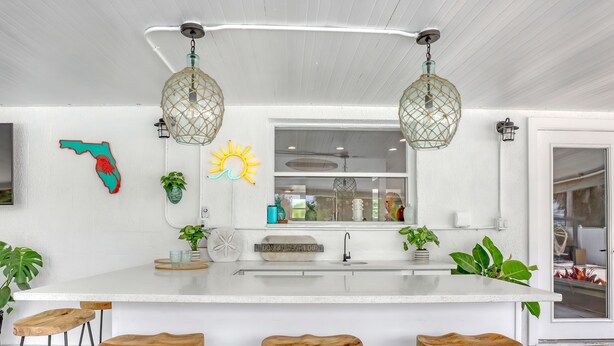 A kitchen with a white countertop, three wooden stools, hanging pendant lights, and a window with a view. - Catalina Hideaway - Heated Pool - Game Room (Indian Harbour Beach)