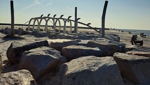 Una playa con rocas grandes, una escultura de metal y un cielo despejado.