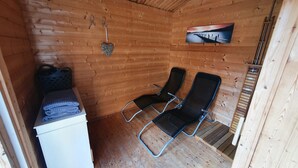 Una cabaña de madera con dos sillas negras, una mesita con toallas y un cuadro de un muelle en la pared.