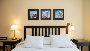 Een hotelkamer met een bed, twee nachtkastjes met lampen, een bijzettafeltje en drie ingelijste foto's aan de muur.