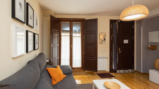 Een woonkamer met een grijze bank, een witte salontafel en een geweven hanglamp.