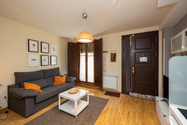 A living room with a grey sofa, orange cushions, a white coffee table, and a hanging light fixture. - Casa Benito. EN EL Corazón DEL Casco Histórico (Zamora)
