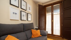 Een woonkamer met een grijze bank, oranje kussens en ingelijste foto’s aan de muur.