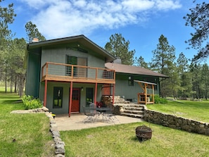 A two-story house with a balcony, stone steps, and a patio area with outdoor furniture.