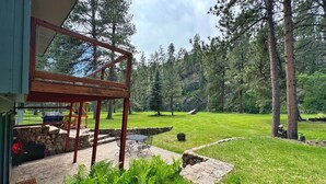A modern house with a stone patio, outdoor seating, and a view of a forested area. - Secluded Setting On French Creek In The Southern Black Hills (Custer)