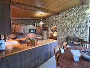 A kitchen with wooden cabinets, a stone wall, a wooden ceiling, and a dining area with a table and chairs.