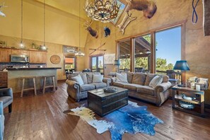 A spacious living area with a large sofa, a coffee table, and a rustic ceiling with animal taxidermy. - Hitchin Post - Firepit, hot tub, Access to Pool! (Lead)