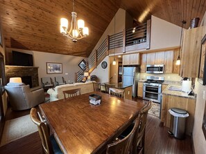 Uma cozinha ampla com armários de madeira, uma área de refeições com mesa de madeira e uma escada que dá acesso a um andar superior.