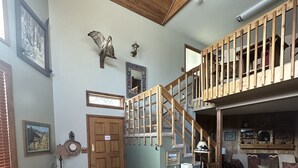 Un salon spacieux avec un escalier en bois, un canapé en cuir noir, une table basse en bois et une cheminée accueillante.