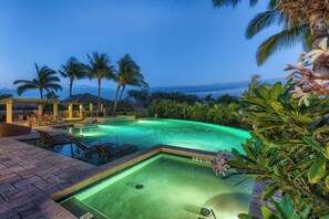 Un área de piscina con sillas de descanso y un pabellón, rodeado de palmeras y plantas tropicales.
