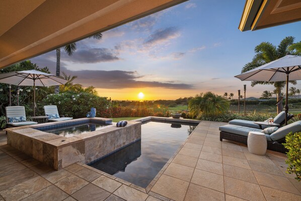 Zona de piscina con sillas de descanso y sombrillas, rodeada de vegetación y vistas al atardecer.
