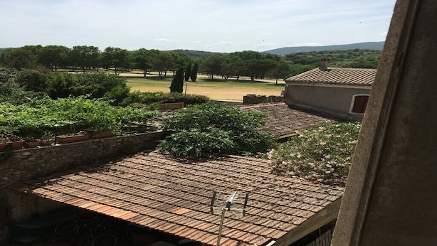 Vista desde una ventana que da a un patio con tejado de tejas, pared de piedra y zona ajardinada con árboles.
