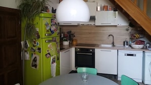 Una cocina compacta con un refrigerador verde, armarios blancos, una escalera de madera y un comedor con mesa y sillas.