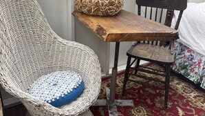 Une chaise en osier avec un coussin bleu, une table en bois avec un panier tressé, et une chaise en bois foncé recouverte d’une housse à motifs floraux.