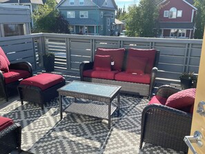 A patio with wicker furniture, a patterned rug, and a view of houses in the background.