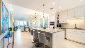 A modern kitchen with a central island, bar stools, pendant lighting, and white cabinetry. - Beachcomber 3 by Grand Cayman Villas (7 Mile Beach)