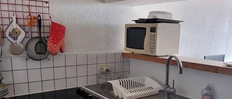 Een kleine keuken met een fornuis, oven, magnetron, spoelbak en een rode prullenbak.