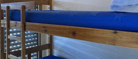 Una cama litera con ropa de cama azul, estructura de madera y ventana con persianas.