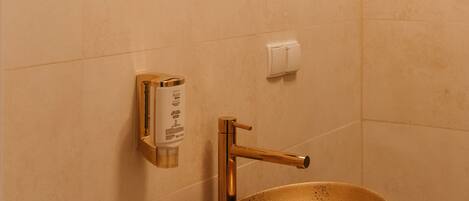Une salle de bain avec un miroir rond, un lavabo doré et un distributeur de savon fixé au mur.