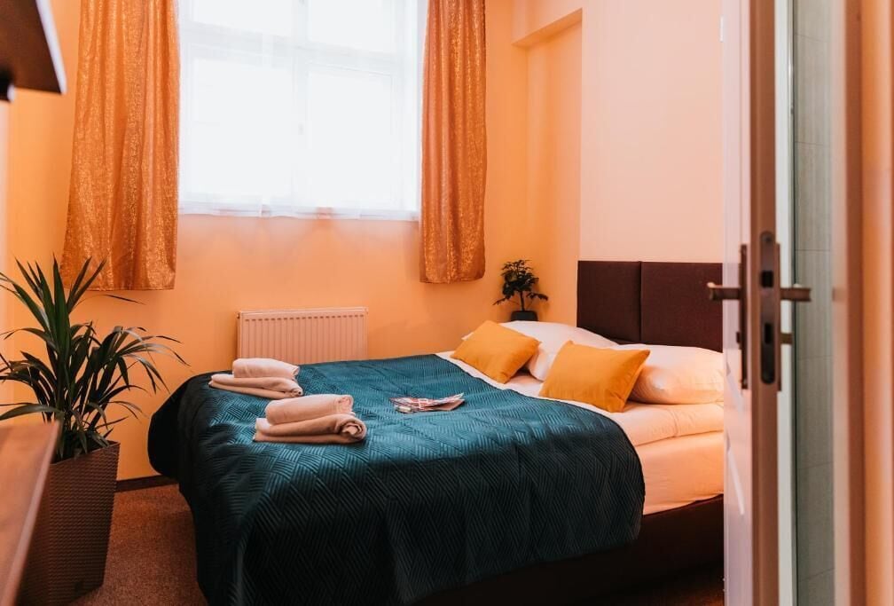 A neatly made bed with a teal bedspread, two pillows, and folded towels on the side.
