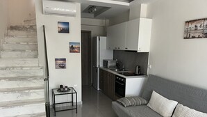 A modern kitchen with a built-in microwave, oven, and sink. There's a grey sofa with striped pillows and a small side table with two candles. - Vero Resort Townhouse Hanioti (Халкидики)